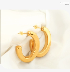Macro shot of polished gold-plated thick C-shape hoop earrings on white silk fabric