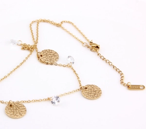 Macro detail of hammered stainless steel disc and sparkling zircon pendant on gold chain