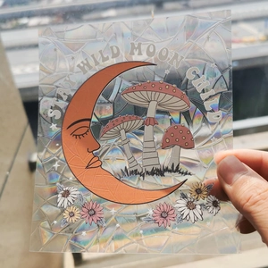 Detailed holographic suncatcher sticker featuring crescent moon and mushrooms held in hand