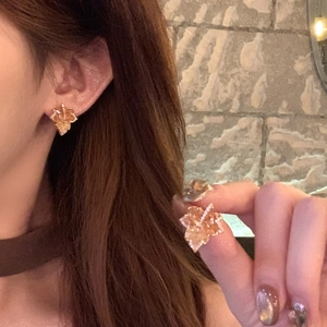 Elegant maple leaf gold-plated stud earrings with pavé zircons worn by a female model