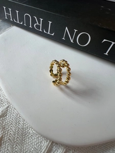 Dettaglio macro di un anello a doppia fila di perline dorate su vassoio in pietra