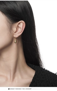Close-up of model wearing minimalist gold teardrop earrings with a polished metallic finish