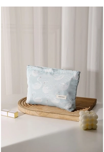 Detail of mint green makeup bag with swan jacquard pattern on a wooden tray
