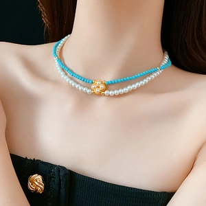 Dettaglio della collana a due strati con perle blu e ciondolo a quadrifoglio d'oro