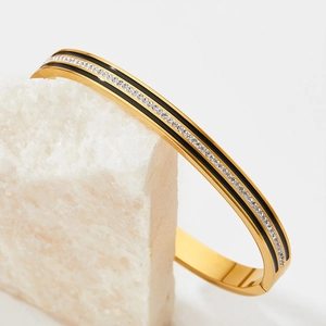 Elegant gold bangle with black enamel and sparkling zircons on white crystal stone