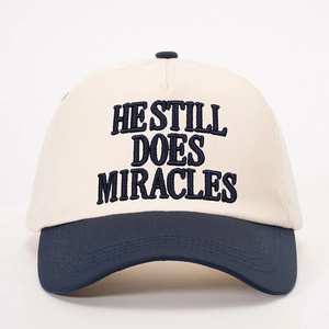 Adjustable two-tone baseball cap with HE STILL DOES MIRACLES embroidery on white background