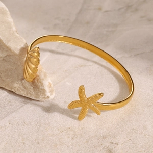 Detailed view of gold starfish and seashell charms on an open stainless steel cuff bracelet
