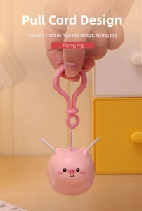 Handheld view of pink flying pig keychain showing mechanical pull-string wing movement