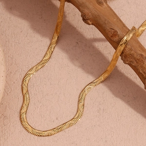 Detailed close-up of golden flat herringbone snake chain necklace on a wood branch