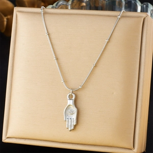 Silver Hamsa Hand pendant necklace with golden eye on bamboo chain displayed on gold cushion