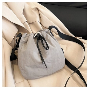 Detail of grey nylon bucket bag with drawstring closure on beige trench coat