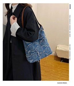 Detail of blue denim tote bag with white flower embroidery and brown leather shoulder strap