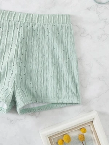 Detail of mint green pointelle knit shorts with elastic waistband on marble surface