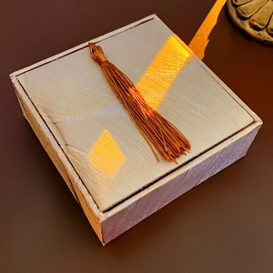 Silver square jewelry gift box with a luxury golden tassel on a minimalist dark surface