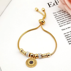Adjustable gold snake chain bracelet with evil eye pendant and crystal beads on a book