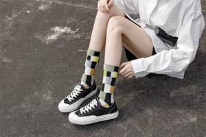 Detail of colorful checkered cotton crew socks shown on a model sitting outdoors