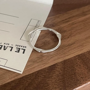 Makroaufnahme eines silbernen, unregelmäßigen Wellenrings auf strukturiertem Holz