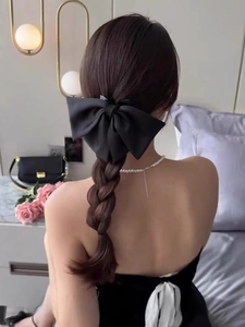Detail of a large black satin bow hair clip styled on a braid with a french elegant look