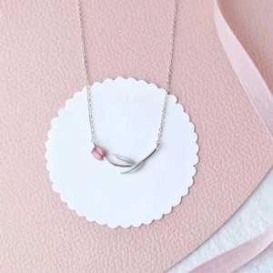 Close-up of a silver tulip necklace pendant with pink petals and green leaves on white card