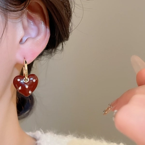 Close-up of heart-shaped gold earring with reddish-brown enamel and inlaid diamonds