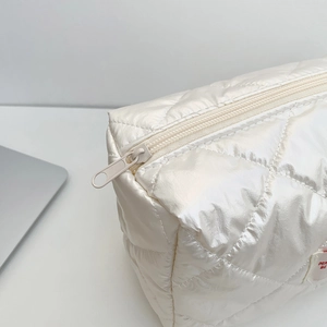 Close-up of white quilted puffer cosmetic bag with smooth zipper and detailed stitching