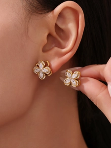 Close-up of sparkling gold clover stud earrings with cubic zirconia on a model's ear