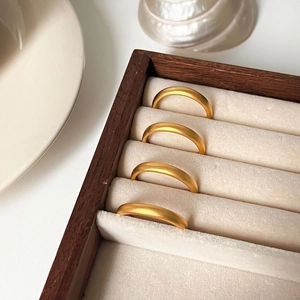 Detail of four matte gold minimalist rings arranged in a wooden jewelry display box