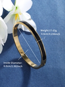 Detailed macro view of a gold-tone stainless steel bangle with black enamel on blue velvet