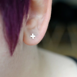 Silver cross stud earring in titanium steel worn by a model with purple hair