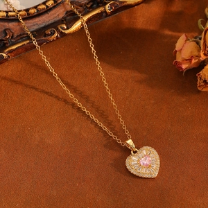 Détail du pendentif cœur doré avec pierre rose et cristaux sur fond de fleurs séchées