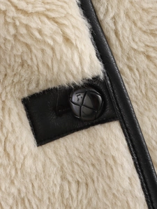 Close-up of beige shearling jacket featuring black leather trim and woven button detail