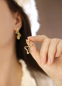 Macro shot of gold stainless steel irregular wave stud earrings with polished finish