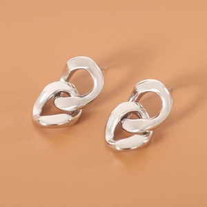 Macro shot of silver intertwined chain link earrings with polished finish on beige surface