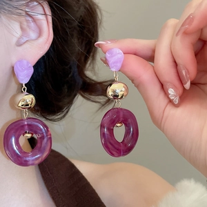 Detail of purple acrylic dangle earrings with golden metal sphere on a model