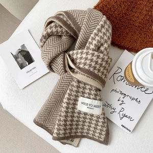 Detailed knit scarf showing houndstooth patterns and a woven brand label on white background