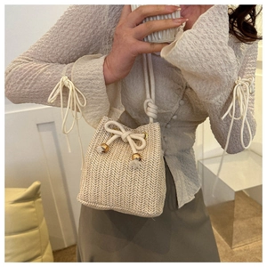 Detail of woven straw bucket bag showing texture, drawstring closure, and metal accents