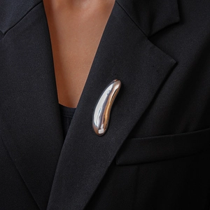 Close-up of a silver teardrop brooch pinned on a black suit lapel with mirror finish