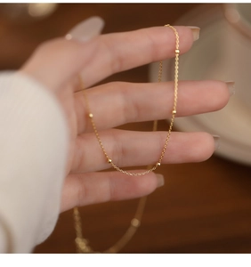 Detail of a minimalist gold beaded silver necklace held in a hand with soft bokeh