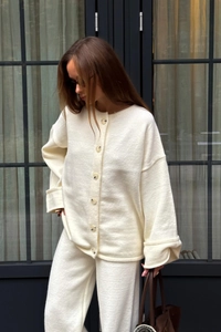 Close-up of cream knit cardigan with amber buttons and matching straight-leg trousers