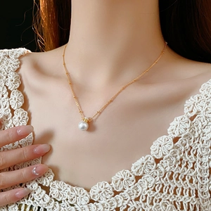 Close-up of gold chain necklace with a single round white pearl pendant on neck