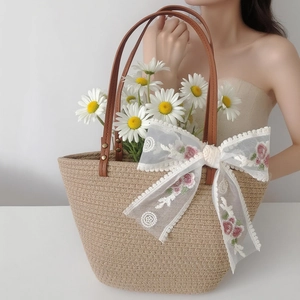 Detail of straw tote bag featuring leather handles and a large floral lace bow accent