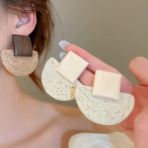 Detailed view of woven raffia and wooden geometric earrings shown on a model for scale