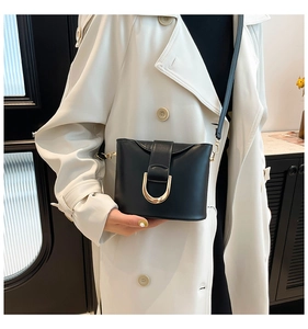 Detail of a chic black PU leather bucket bag with a gold U-shaped buckle on a beige coat