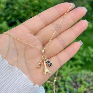 Dettaglio della collana dorata con ciondoli a forma di Torre Eiffel, occhiali e macchina