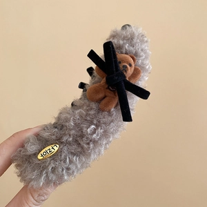 Close-up of a grey plush hair claw clip with a cute brown teddy bear and golden brand tag