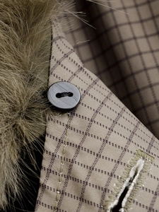 Macro detail of plaid trench coat with black button and soft faux fur collar texture