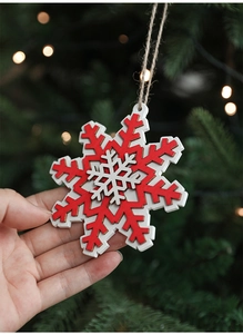 Close-up of a three-layer red and white wooden snowflake ornament held by hand for display