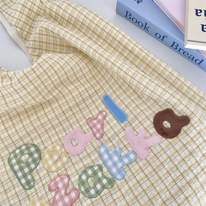 Detail of yellow plaid tote bag with colorful macaron letter embroidery and cotton texture