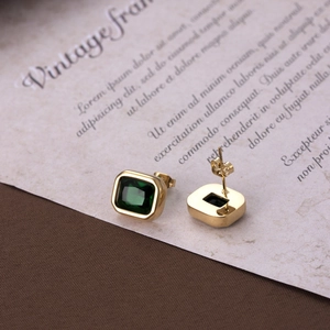 Elegant gold titanium earrings with rectangular green zircon on vintage paper background