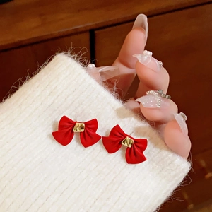 Close-up of red bow earrings with gold accents pinned on white knit fabric background